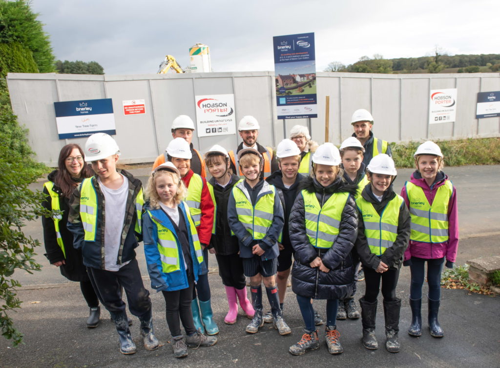 Children in hivis and hardhats in front of the new property development in marton cum grafton