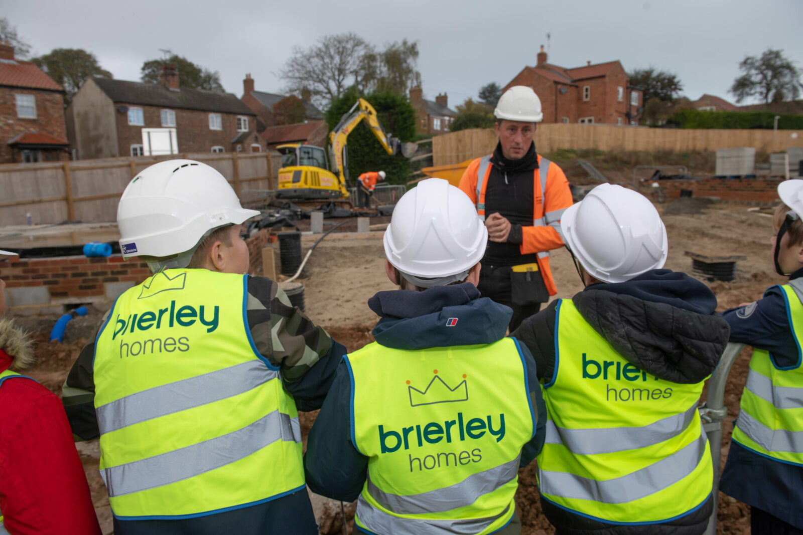 Man in a hardhat speaking to children in hard hats at a property development being built