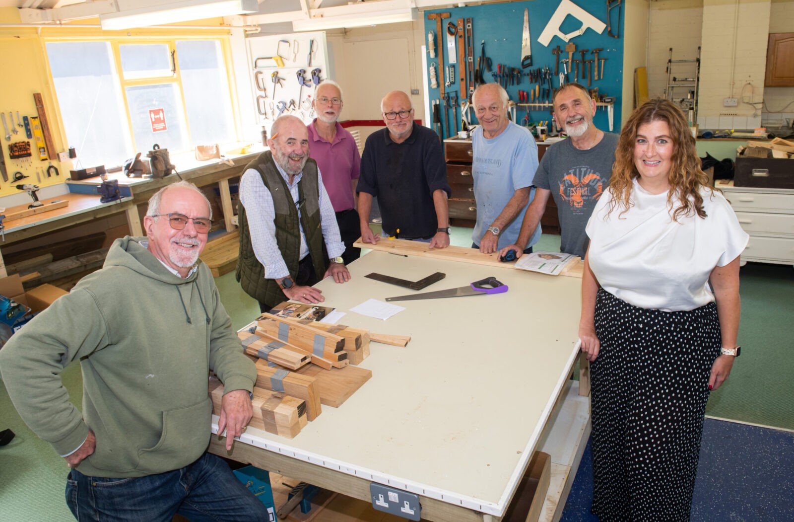 Seven people stood around a table in a work shop